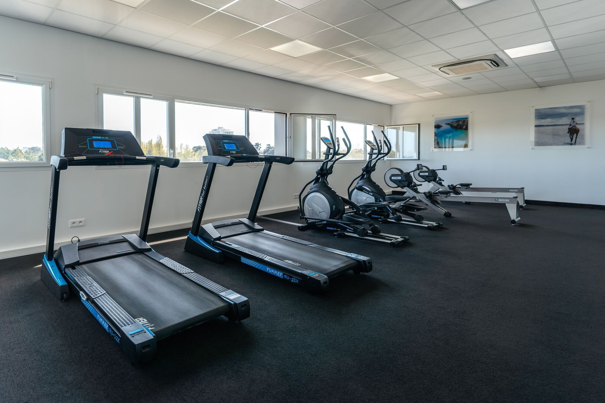 Ein Fitnessraum mit Laufbändern, Crosstrainern und einer Bank.