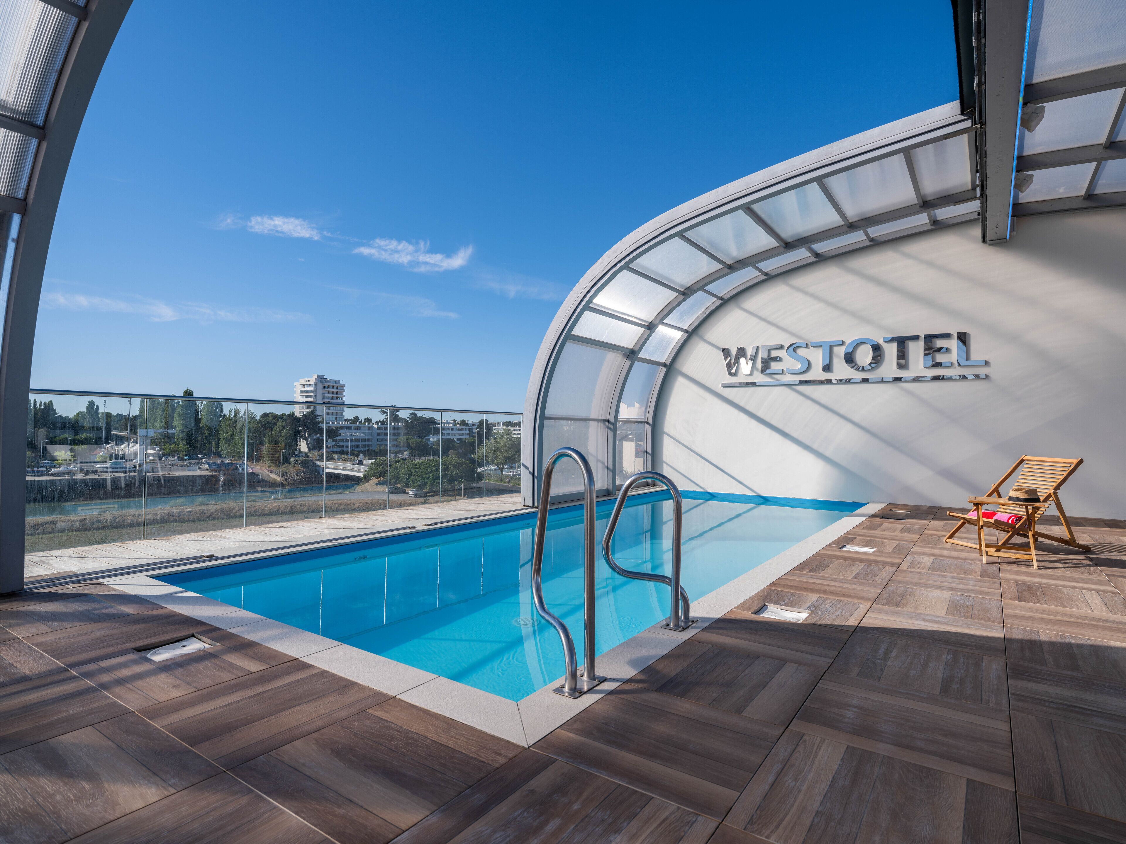 A pool area with a clear view of the cityscape, a wooden deck, and a lounge chair.