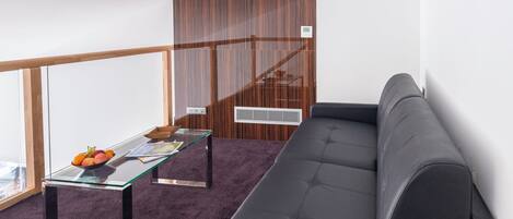 A modern room with a glass-top table, a dark sofa, and a wooden accent wall.
