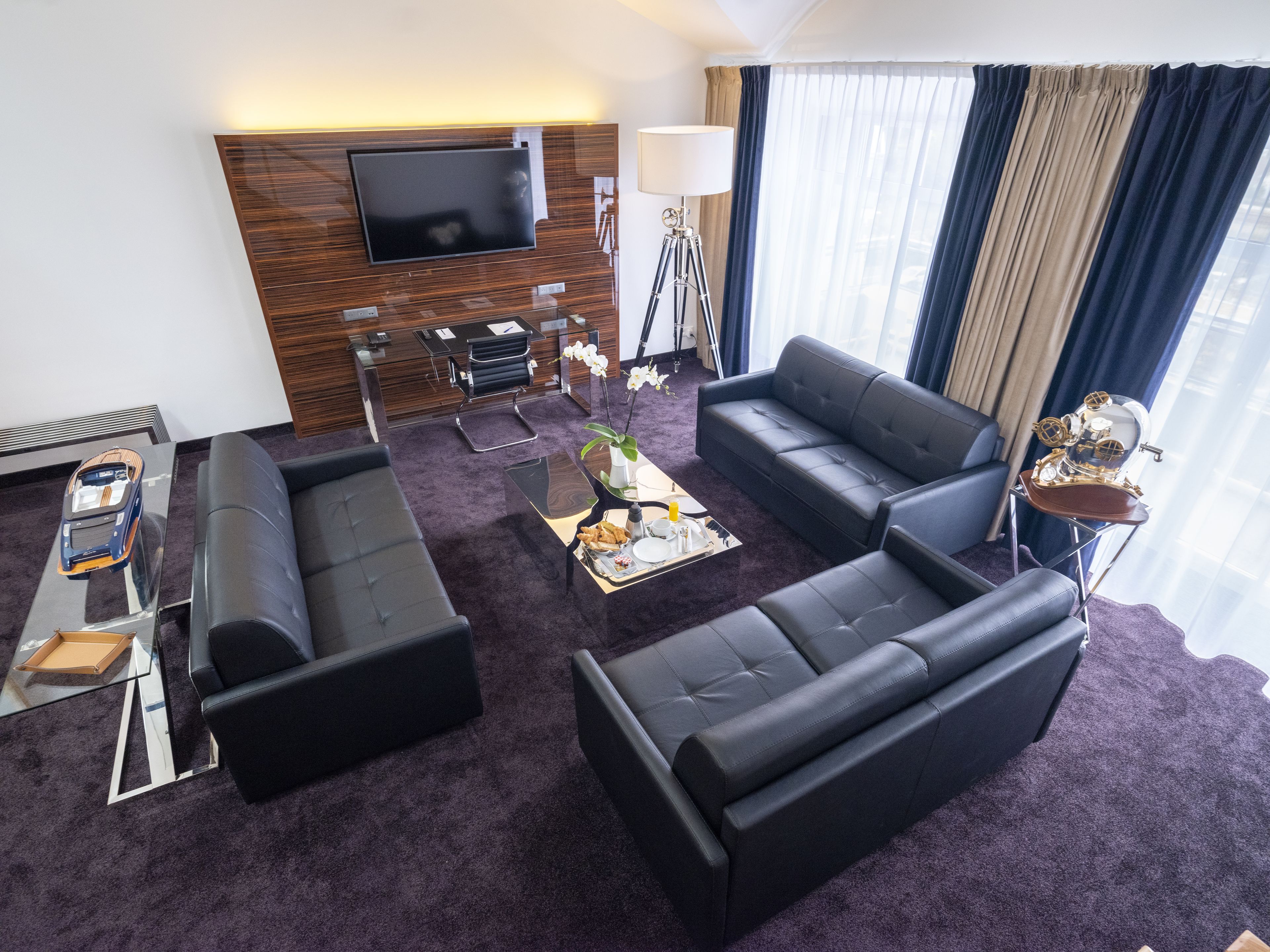 A modern living room with a large flat-screen TV, a sofa, a coffee table, and a lamp.