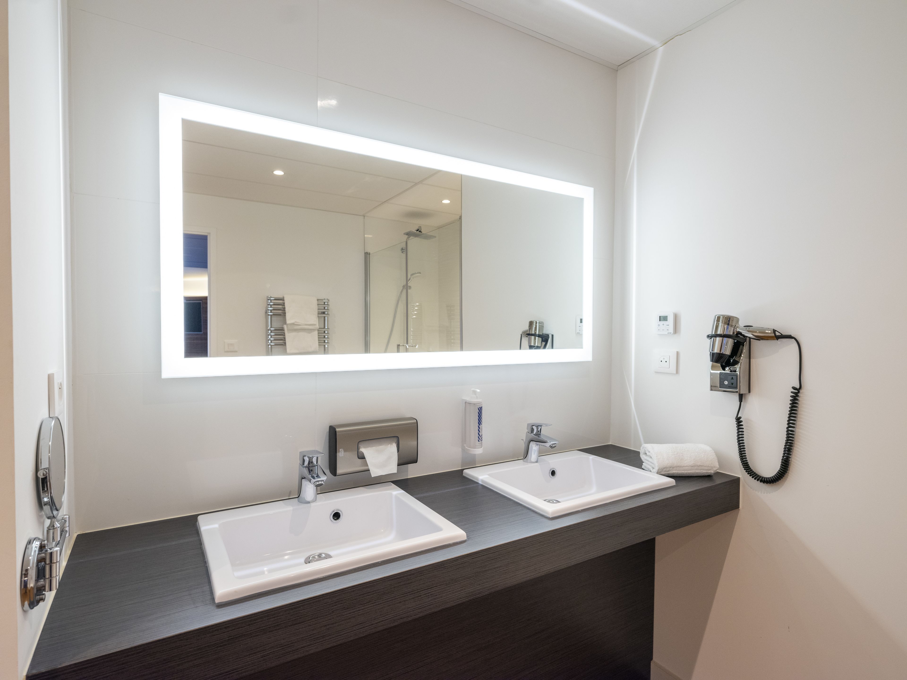 A modern bathroom with two sinks, a large mirror, a hairdryer, and a telephone.