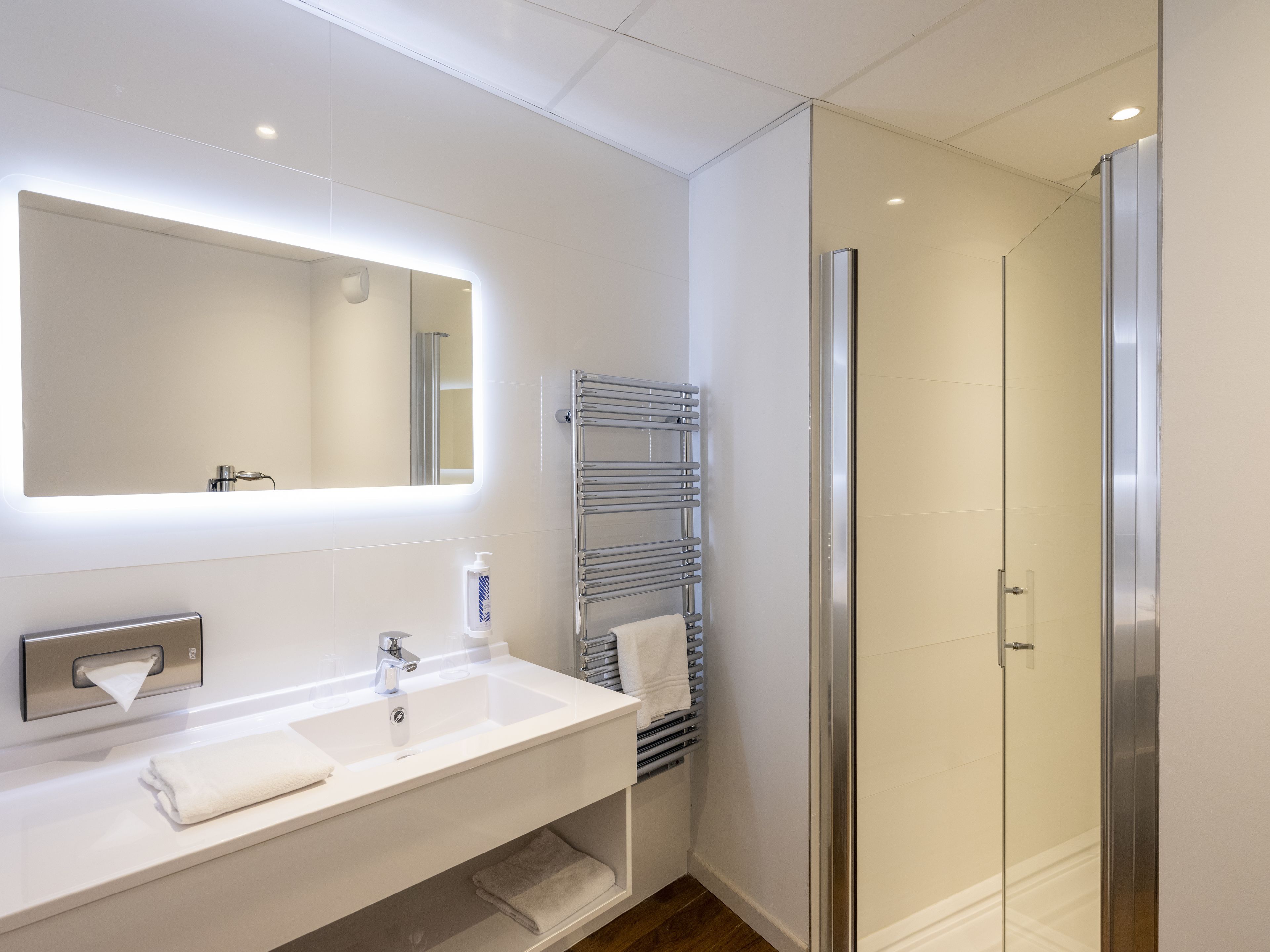 Een moderne badkamer met een witte wasbak, spiegel en handdoekrek.