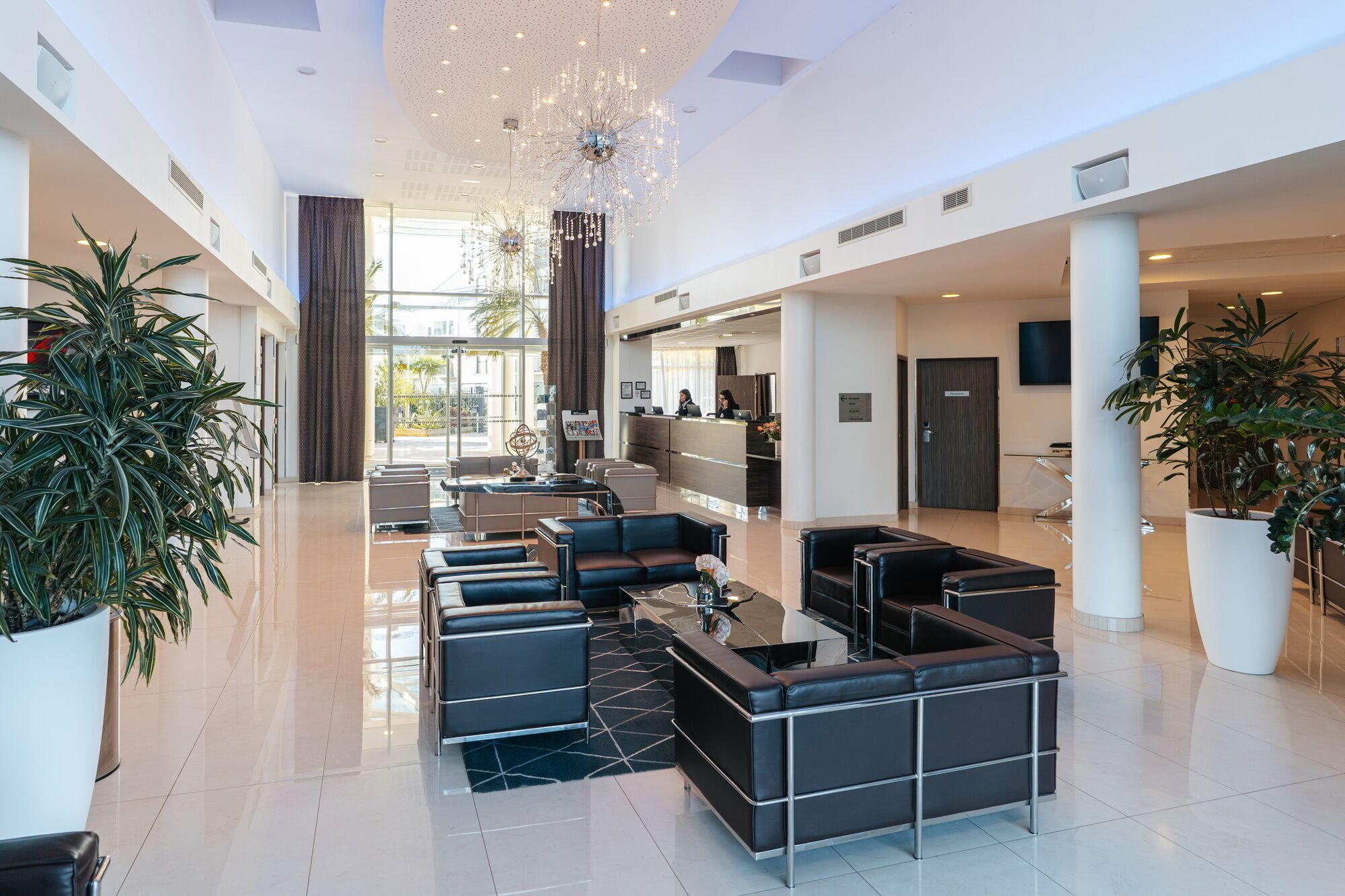 A spacious lobby with a reception desk, seating area, and large potted plants.