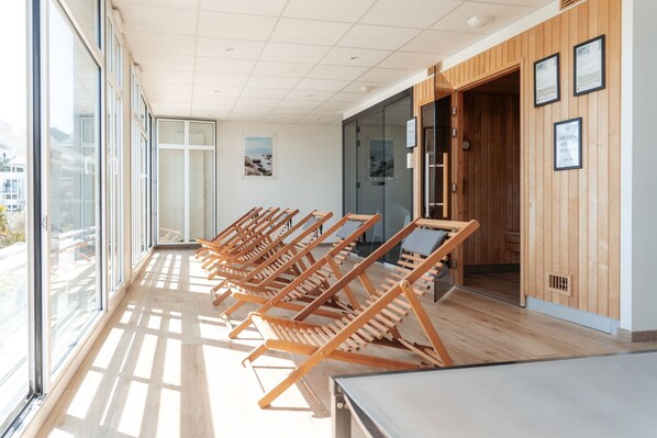 A modern spa room with wooden loungers, large windows, and a view of the outdoors.