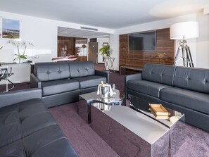 A modern living room with a large flat-screen TV, two black leather sofas, a coffee table, and a small dining area with a table and chairs. - Westotel Le Pouliguen (Le Pouliguen)