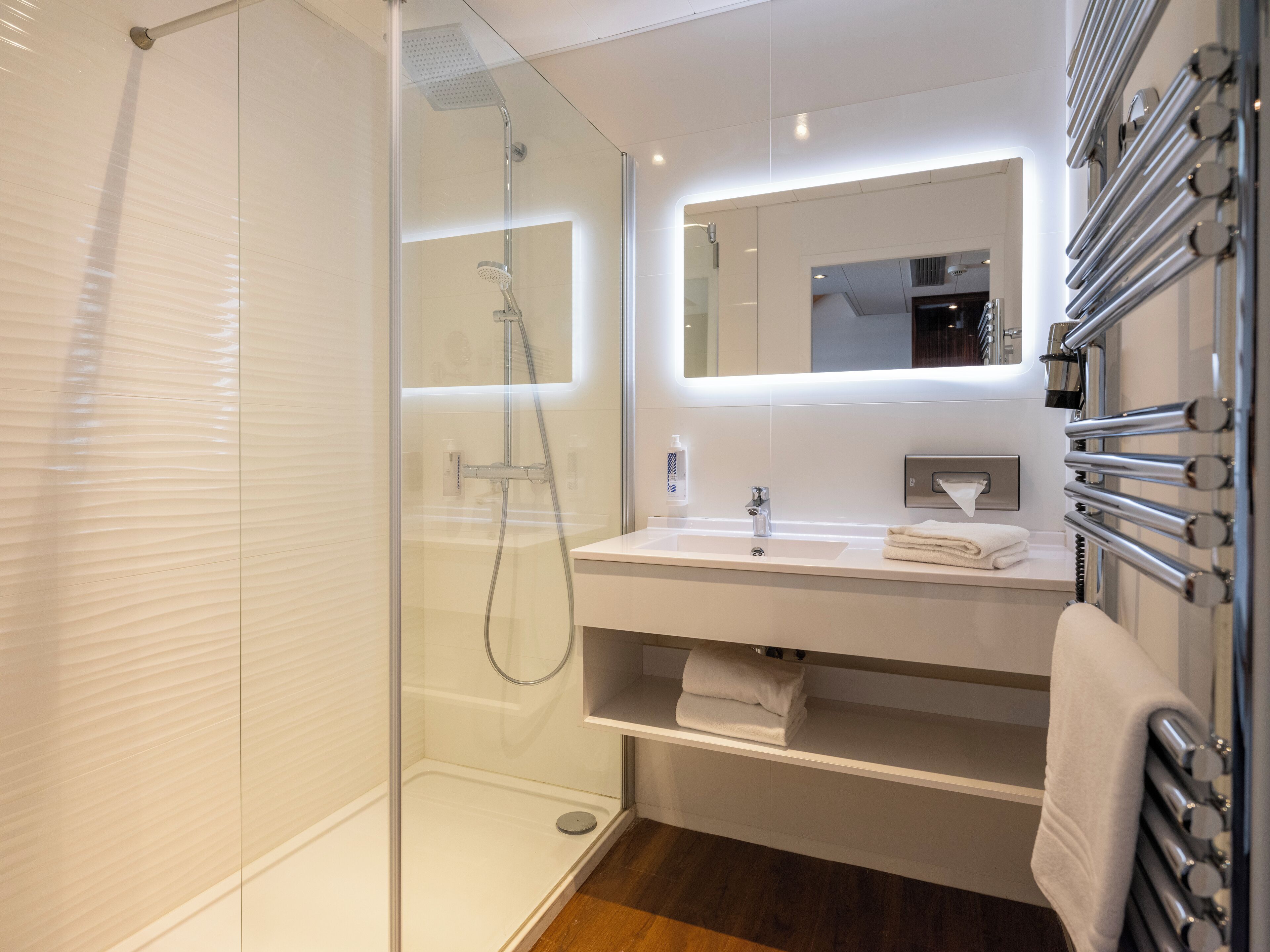 A modern bathroom with a glass-enclosed shower, a white sink with a mirror above it, and a towel rack with towels.