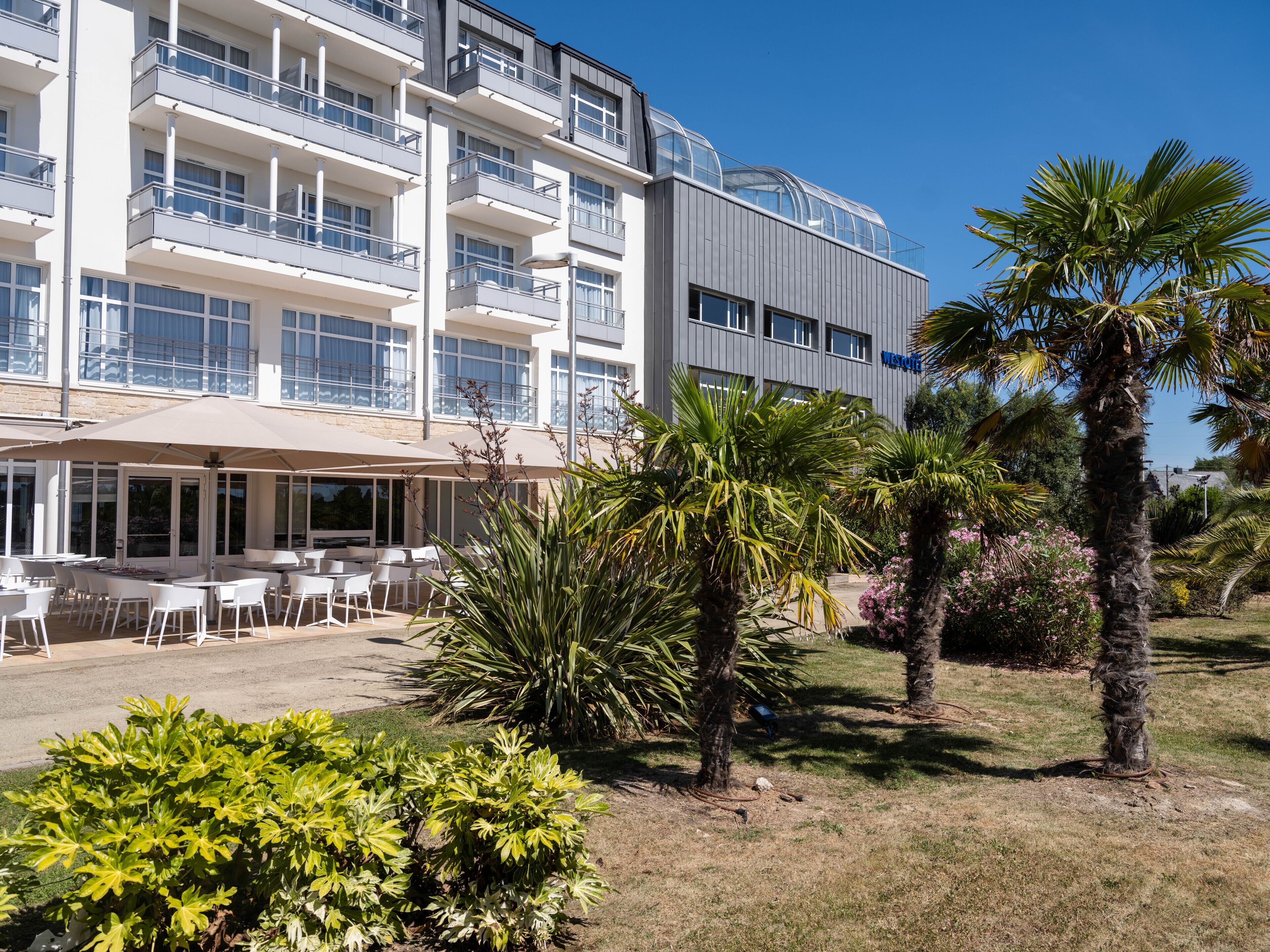 Un hotel moderno con asientos al aire libre y palmeras.