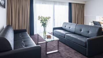 Een moderne woonkamer met een donker leren bank, een glazen salontafel en een bloemenvaas.
