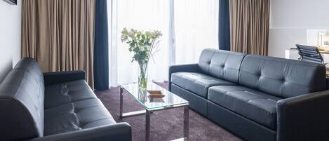 Una sala de estar moderna con un sofá de cuero oscuro, una mesa de centro de vidrio y un jarrón de flores.
