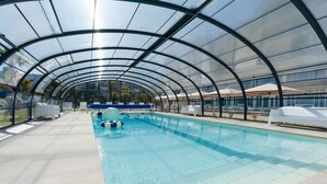 An indoor swimming pool with a glass ceiling, surrounded by white lounge chairs and a blue poolside area. - Westotel Le Pouliguen (Le Pouliguen)