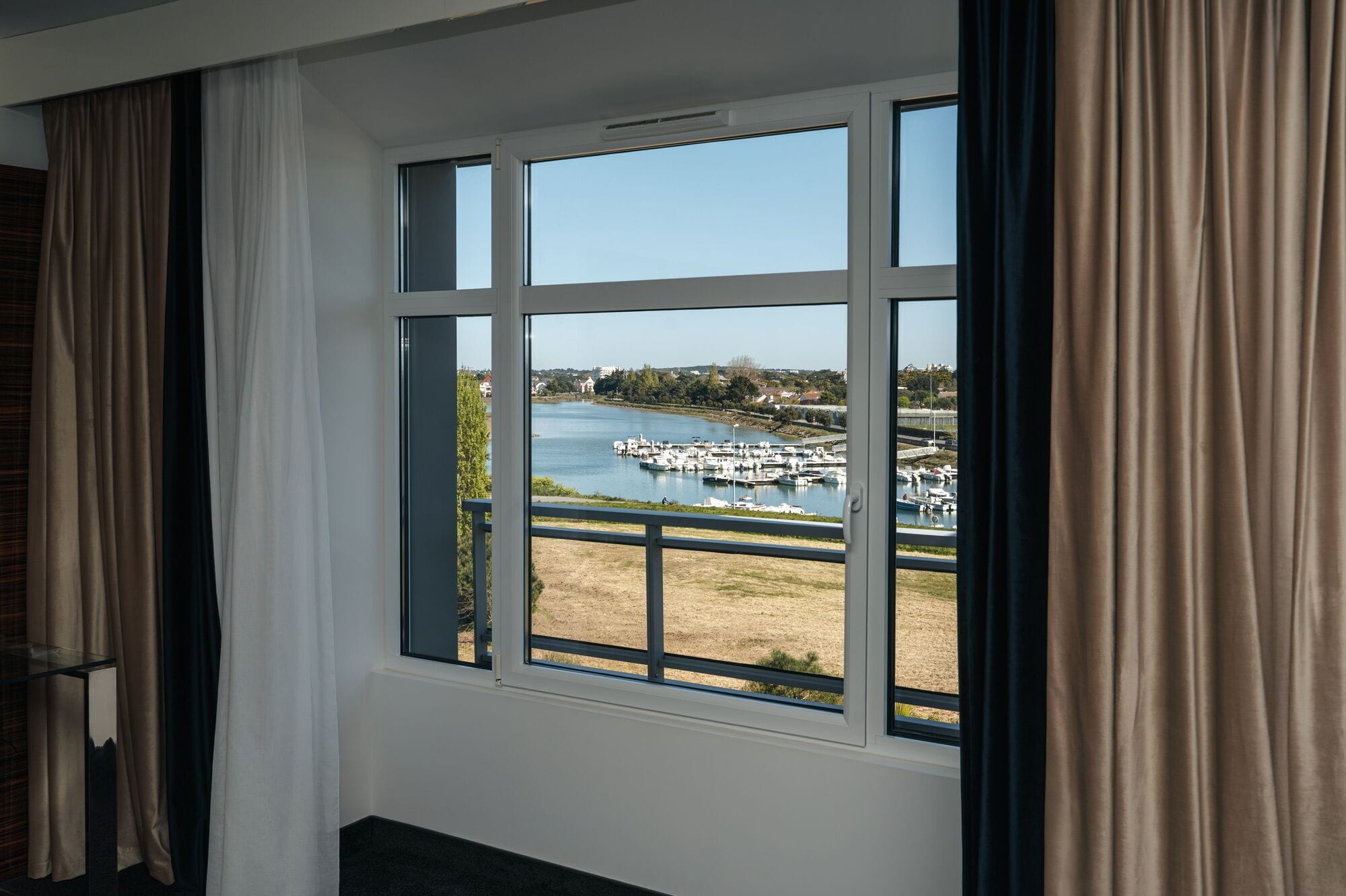 A room with a large window overlooking a marina with boats and a clear sky.