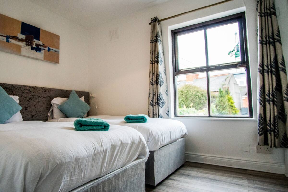 Habitación de hotel con dos camas, una ventana con cortinas y un cuadro en la pared.