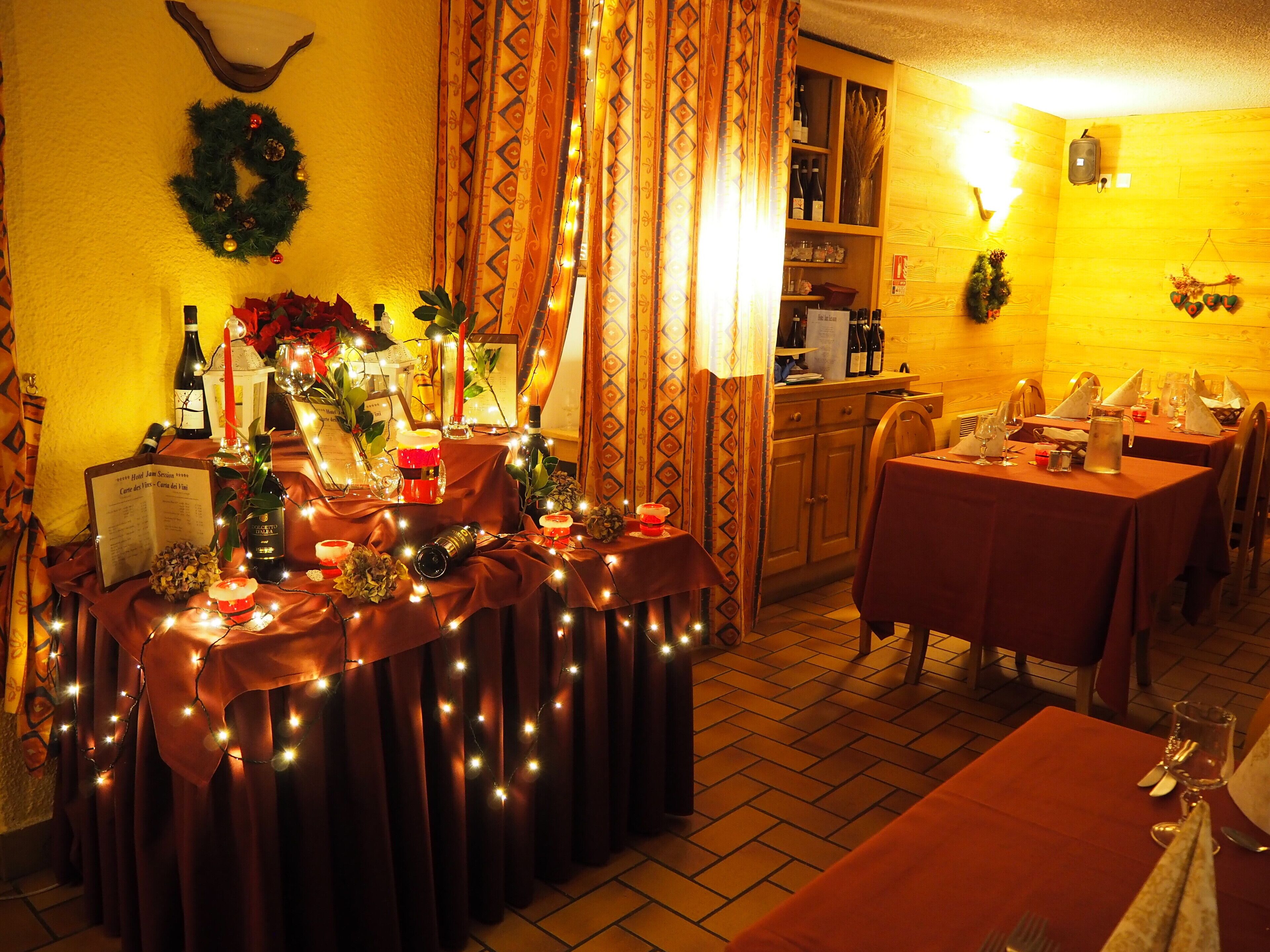 A warmly lit dining area with tables set for a meal, featuring string lights and festive decorations.