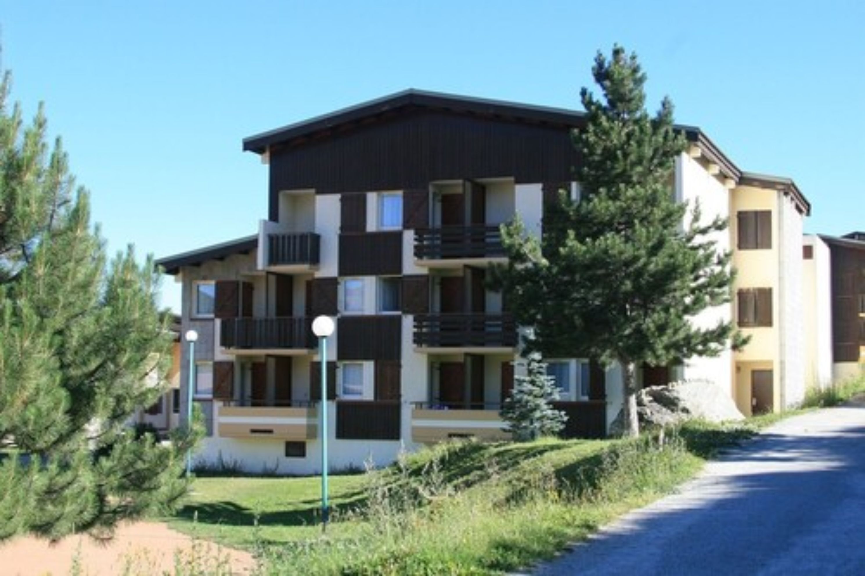 A multi-story residential building with balconies, a clear sky, and surrounding greenery.