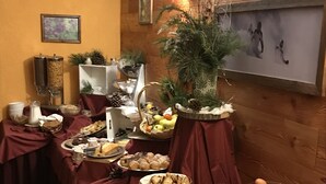 Una mesa de buffet con diferentes alimentos y bebidas, frente a una pared de madera con un cuadro enmarcado.