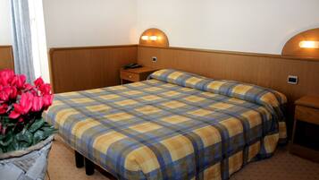 A hotel room with a bed, bedside tables, a lamp, and a vase of flowers.