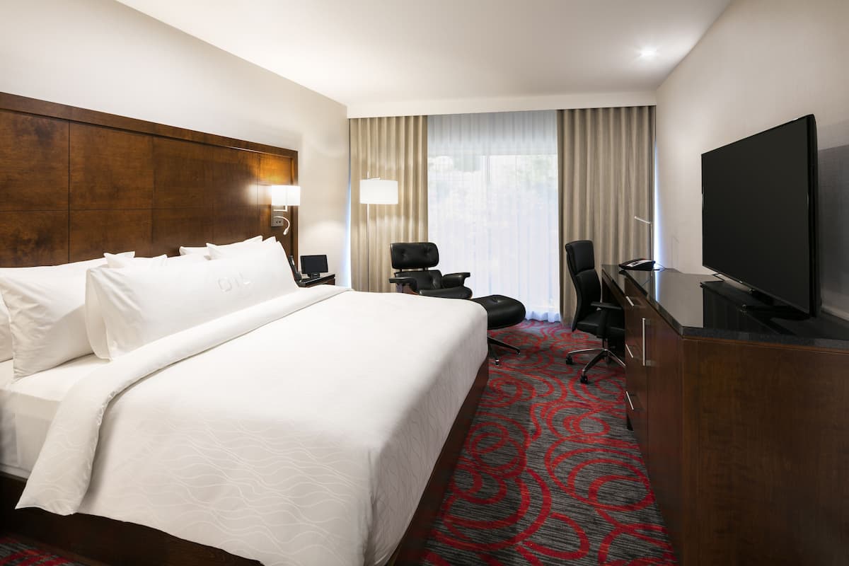 Ein Hotelzimmer mit einem großen Bett, einem Schreibtisch, einem Flachbildfernseher, einem Sessel und einer Lampe.
