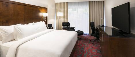 Ein Hotelzimmer mit einem großen Bett, einem Schreibtisch, einem Flachbildfernseher, einem Sessel und einer Lampe.