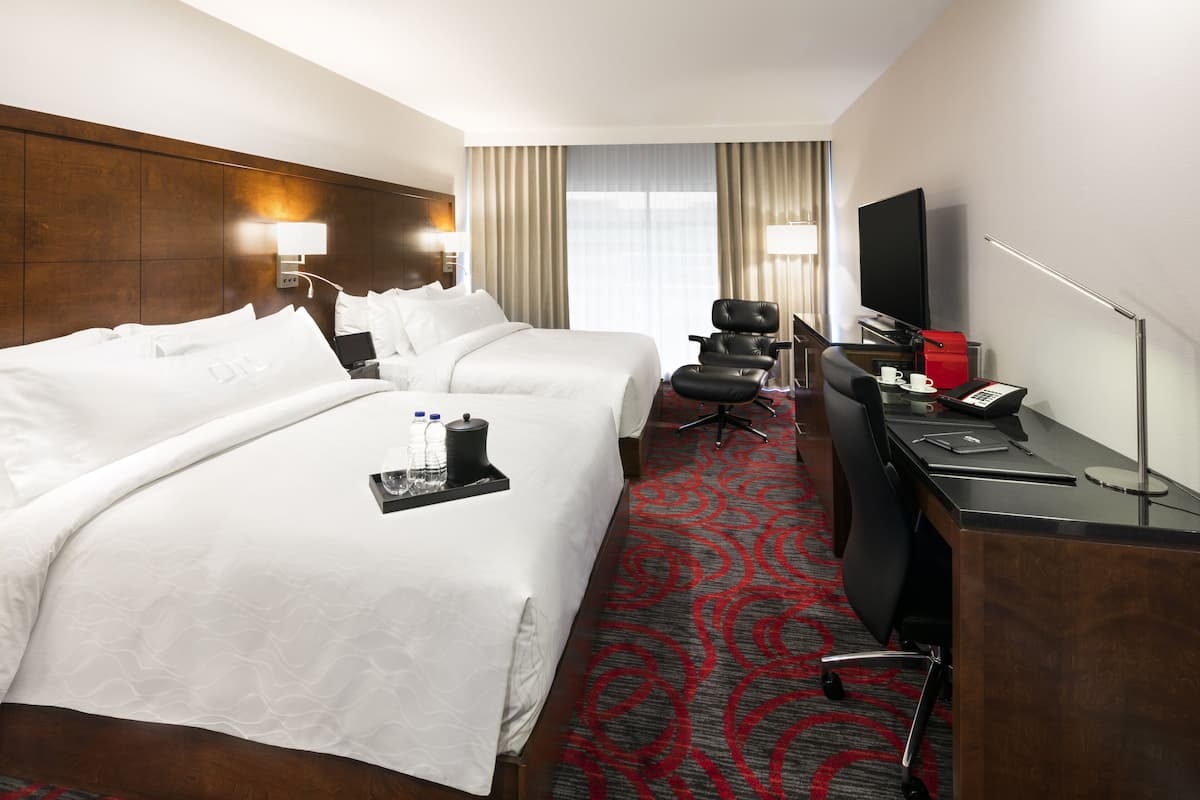 Ein Hotelzimmer mit zwei Betten, einem Schreibtisch mit Computer, einem Fernseher und einer Schreibtischlampe.
