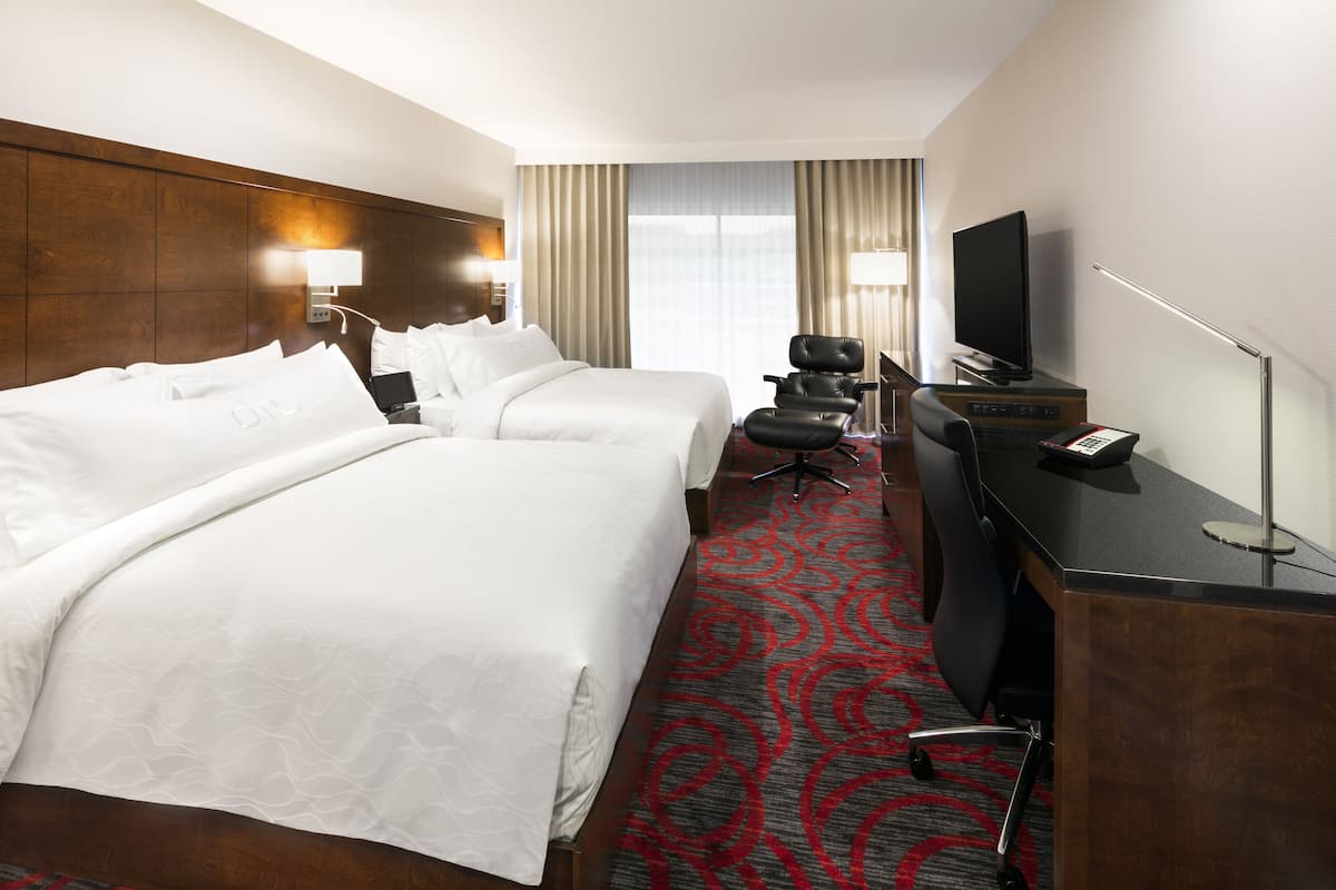Ein Hotelzimmer mit zwei Betten, einem Schreibtisch, einem Computer, einem Fernseher und einer Lampe.