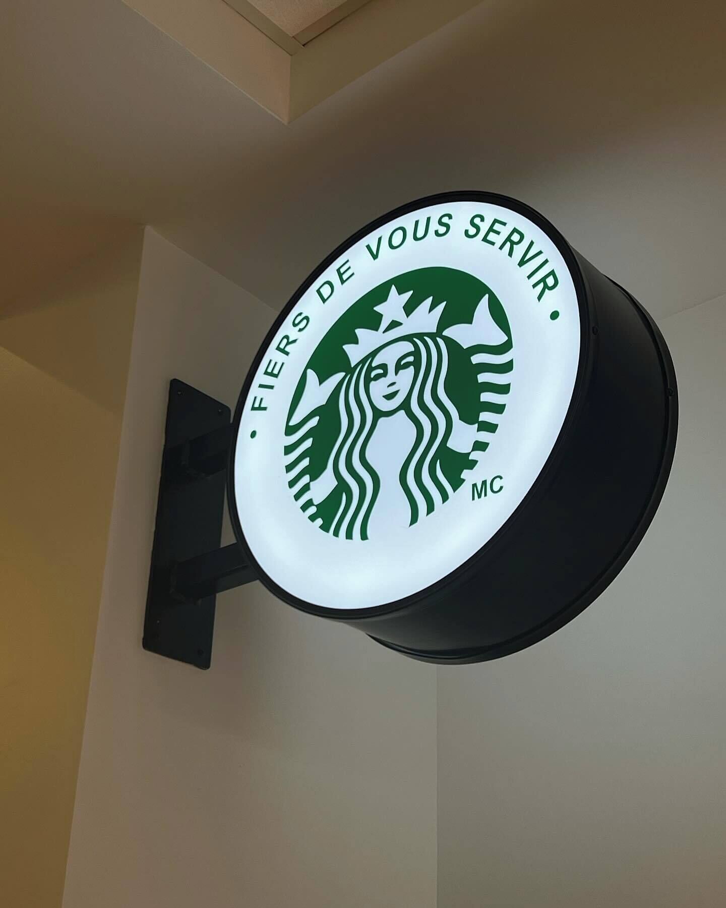 A circular sign with the Starbucks logo and the text "Fiers de vous servir."