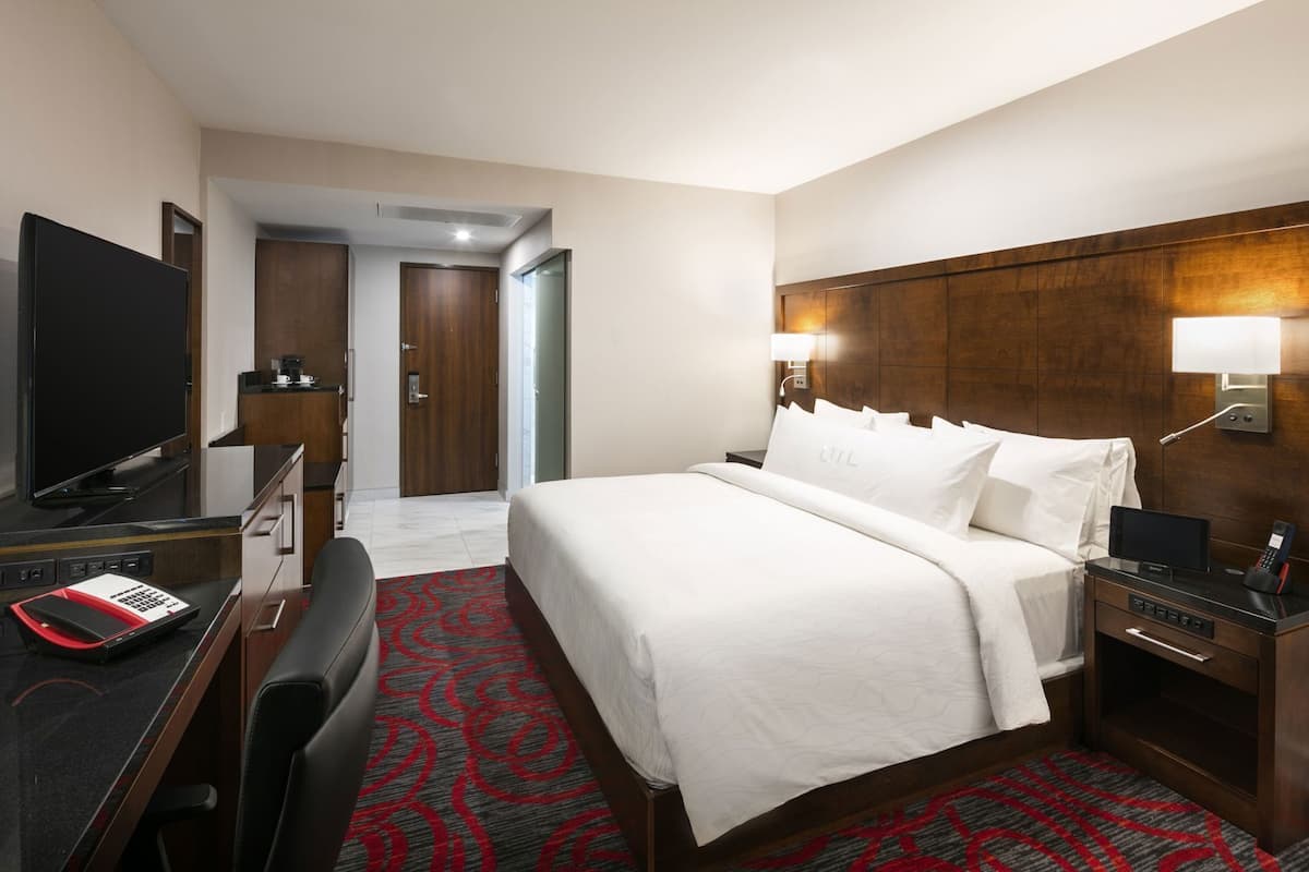 Ein Hotelzimmer mit Bett, Schreibtisch, Fernseher, Telefon und Lampe.