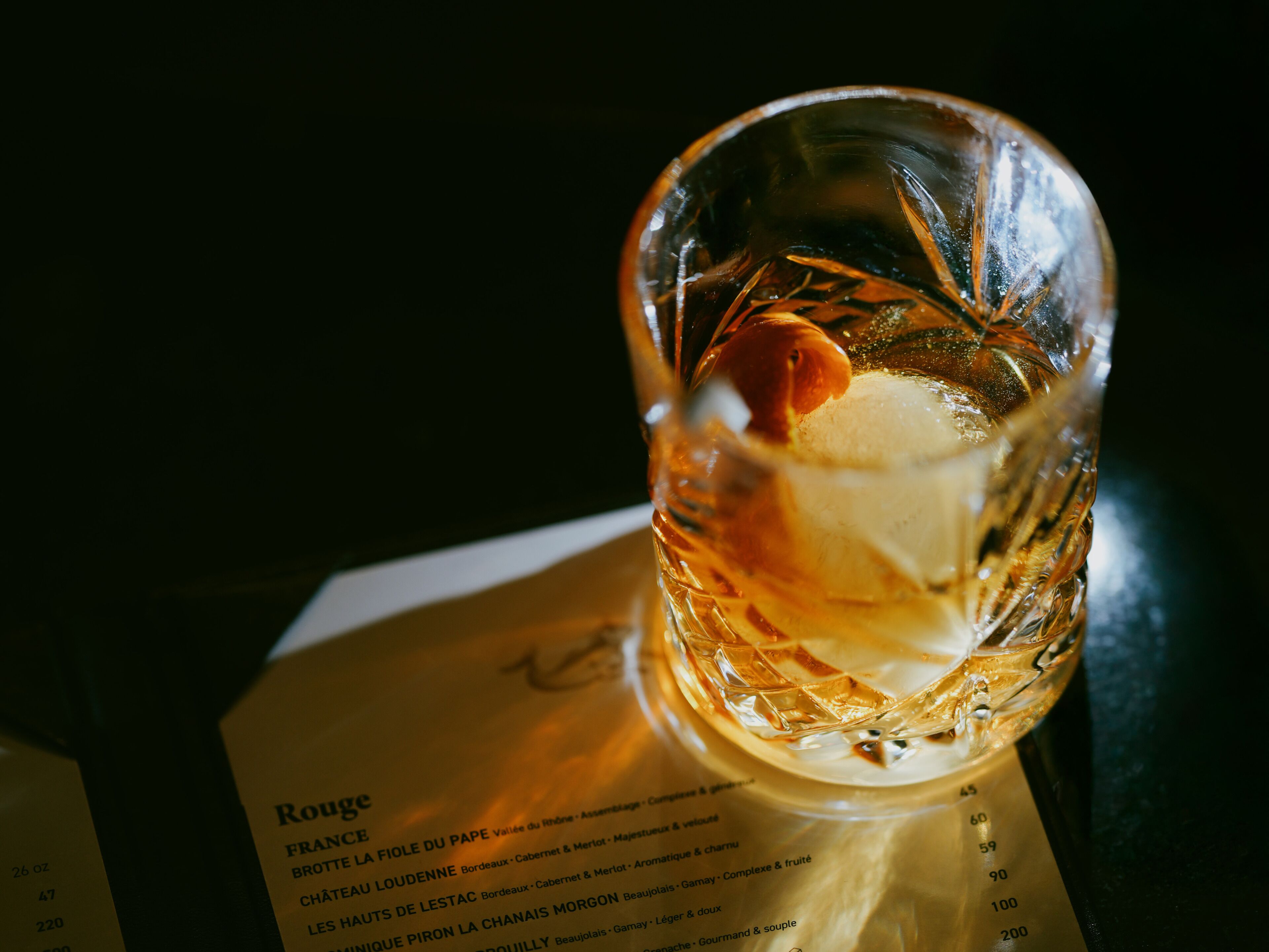 Un menu posé sur une table, accompagné d’un verre contenant une boisson, peut-être un cocktail.