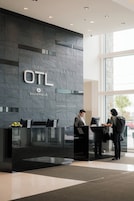 A reception desk with a dark tiled wall, a sign reading "OTL Gouverneur," and two individuals interacting at the counter.