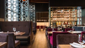Un restaurante con cabinas y mesas, una zona de bar con estantes llenos de botellas, y una pared con un diseño geométrico.