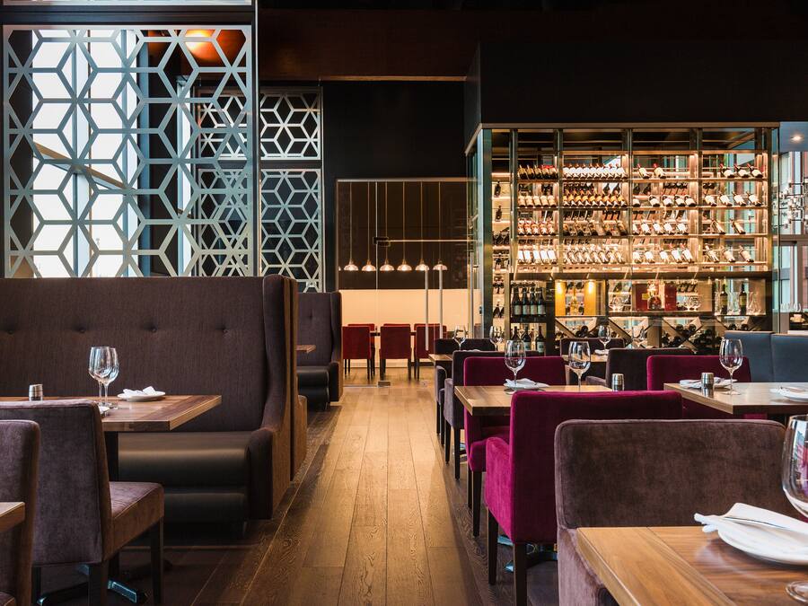A restaurant with booths and tables, a bar area with shelves of bottles, and a geometric patterned wall.