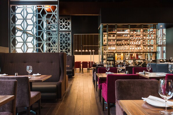 A restaurant with booths and tables, a bar area with shelves of bottles, and a geometric patterned wall.