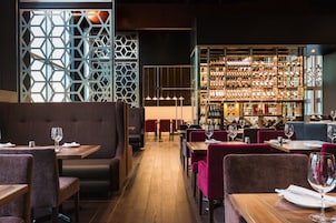 A restaurant with booths and tables, a bar area with shelves of bottles, and a geometric patterned wall.