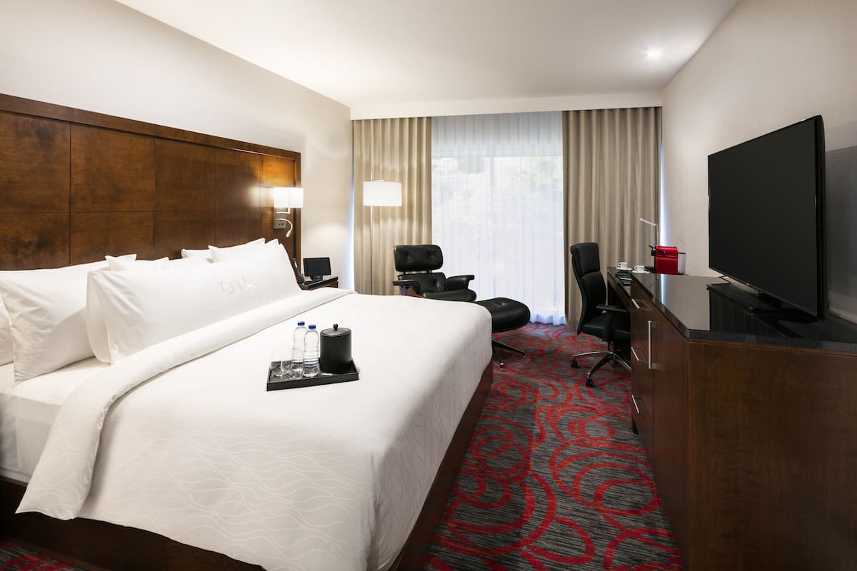 Ein Hotelzimmer mit einem großen Bett, einem Schreibtisch mit Fernseher, einem Stuhl und einer Schreibtischlampe.