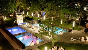 Un área de piscina con varias piscinas, sillas de descanso y una zona con fogata.