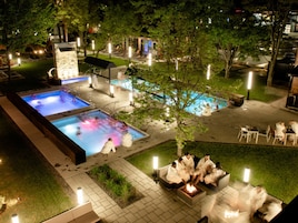 Un área de piscina con varias piscinas, sillas de descanso y una zona con fogata.