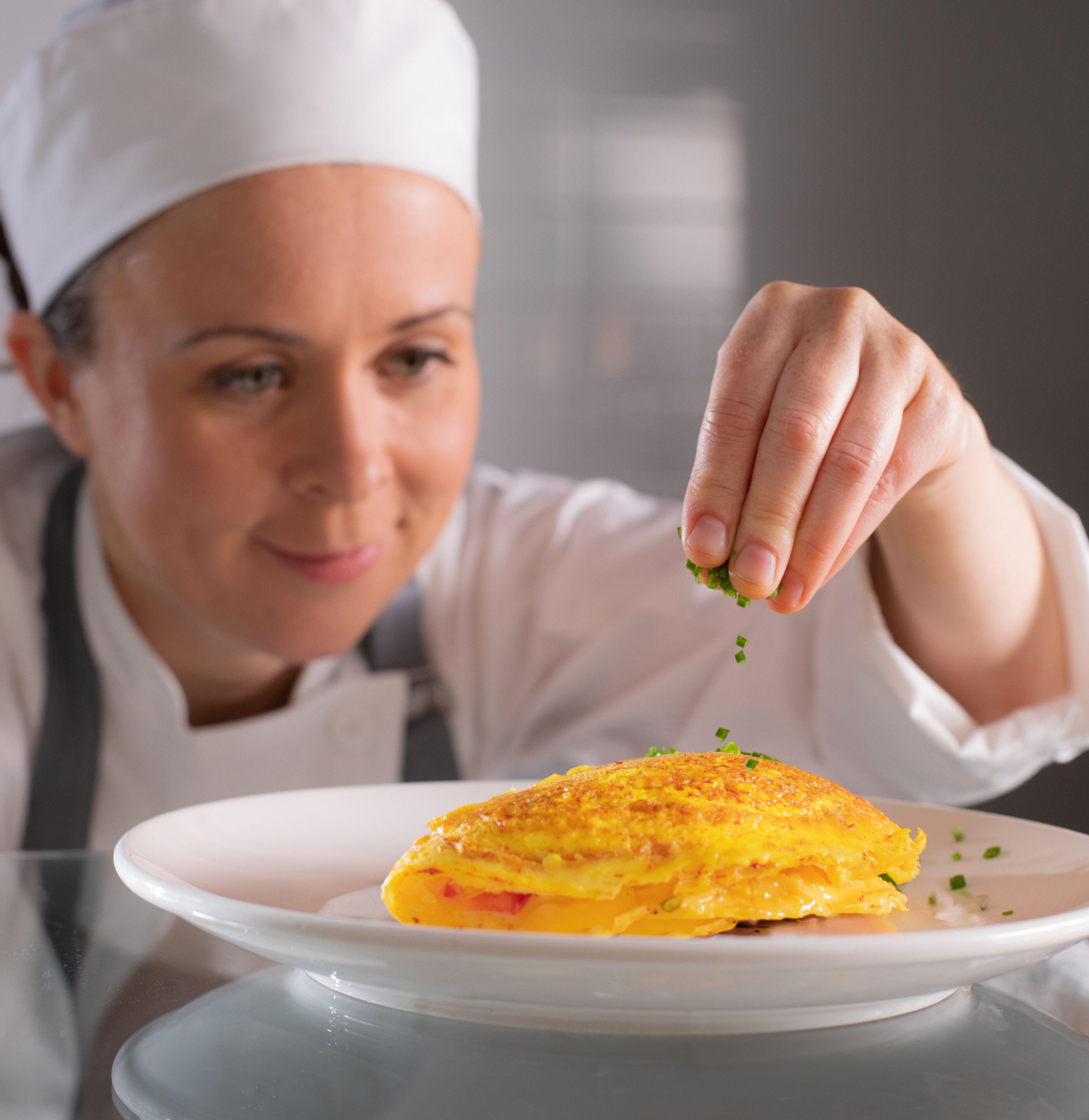 A chef sprinkling green herbs on a dish.