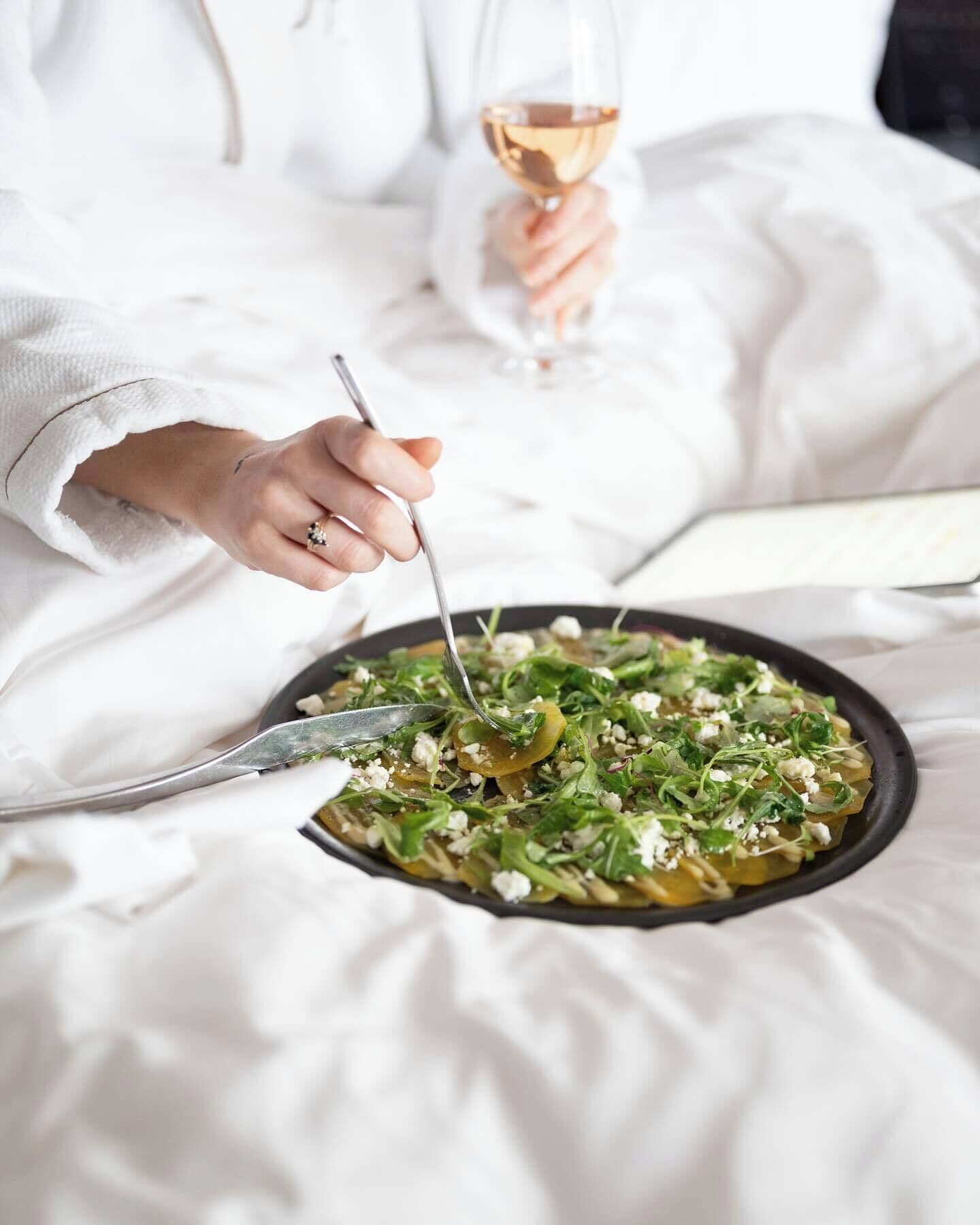 A person in a white robe dining at a table with a salad, holding a fork and a glass of wine.