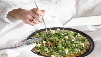 Una persona vestida con una bata blanca comiendo en una mesa, con una ensalada, sosteniendo un tenedor y una copa de vino.