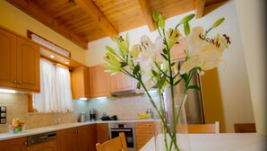 A kitchen with wooden cabinets, a white countertop, and a vase with white flowers. - Villa Milli (Chania)