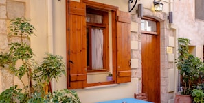 Un edificio rústico con contraventanas de madera, un muro de piedra y macetas con plantas.