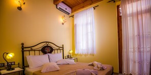 Un dormitorio con cama, dos mesitas de noche, aire acondicionado de pared y una ventana con cortinas de gasa.