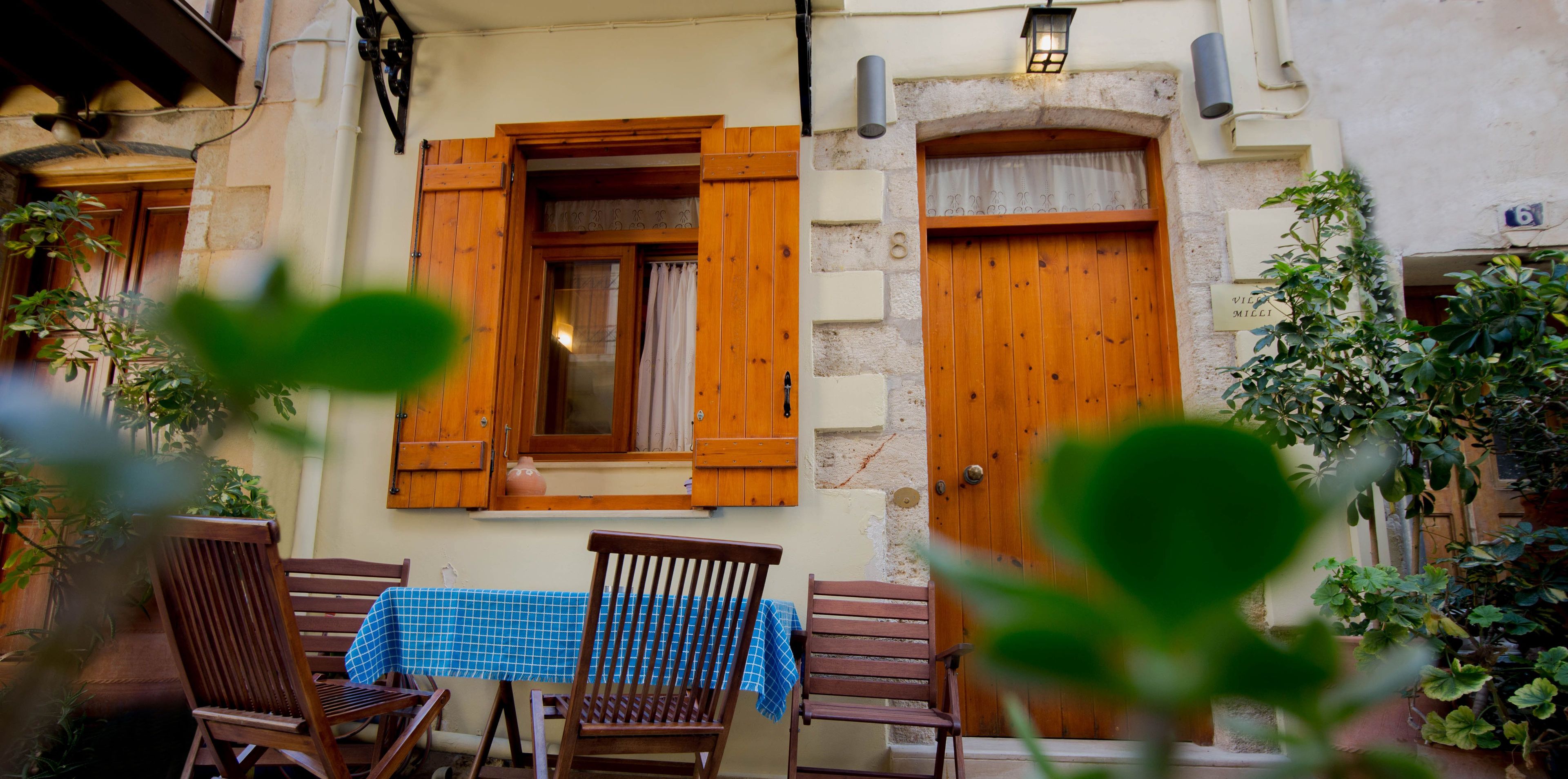 A cozy outdoor seating area with wooden furniture and a table, set against a building with a stone facade and wooden doors.