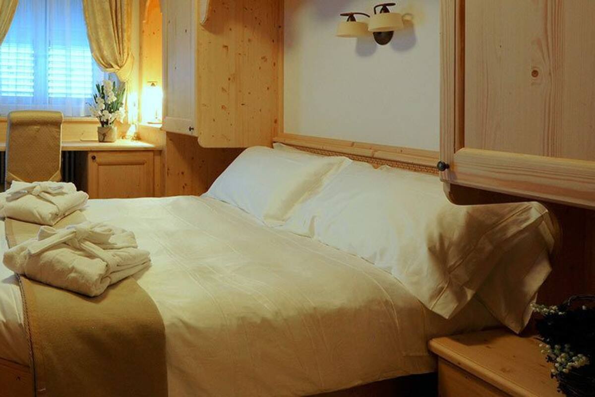 Une pièce aux murs lambrissés, comprenant un lit, un bureau et une fenêtre avec des rideaux.