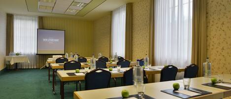 Un salón de conferencias con varias mesas, sillas y una pantalla de proyector que muestra