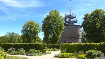 Une tour historique à la base circulaire, dotée d’un escalier en colimaçon, et entourée de jardins et d’arbres bien entretenus.