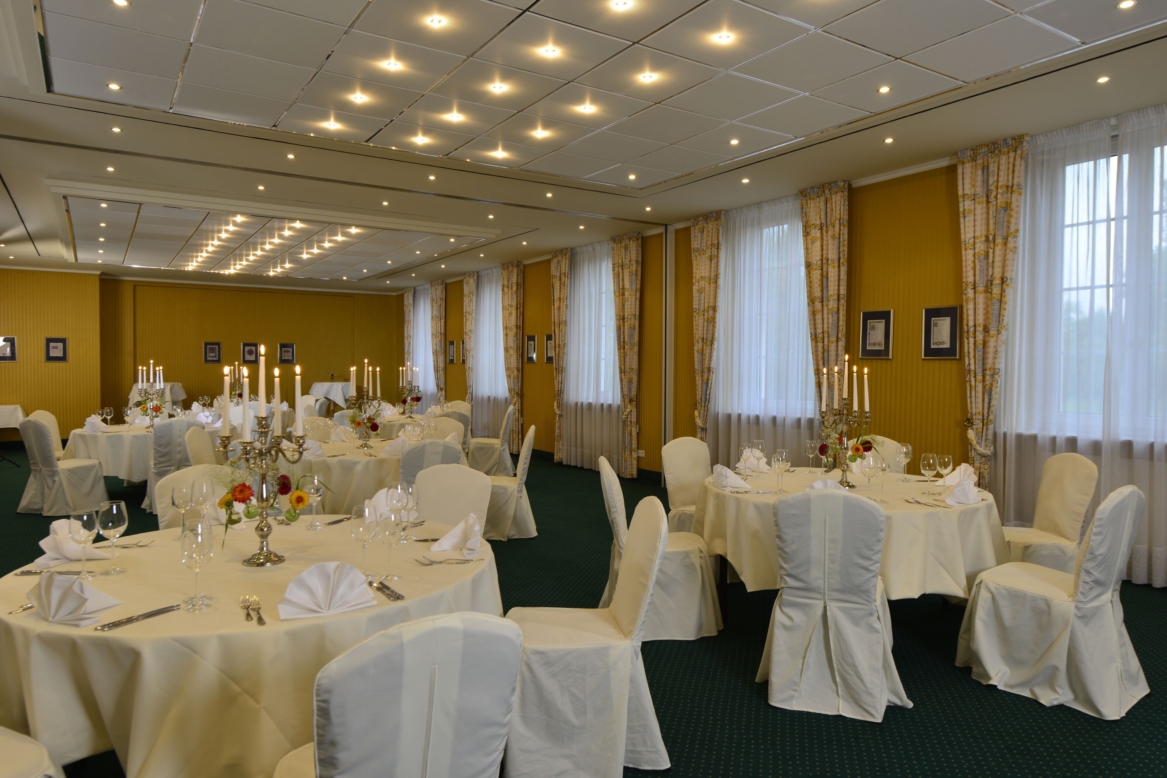 Ein Festsaal mit runden Tischen, weißen Tischdecken und Stühlen mit weißen Bezügen.
