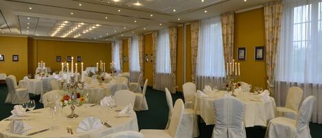 A banquet hall with round tables, white tablecloths, and chairs with white covers.