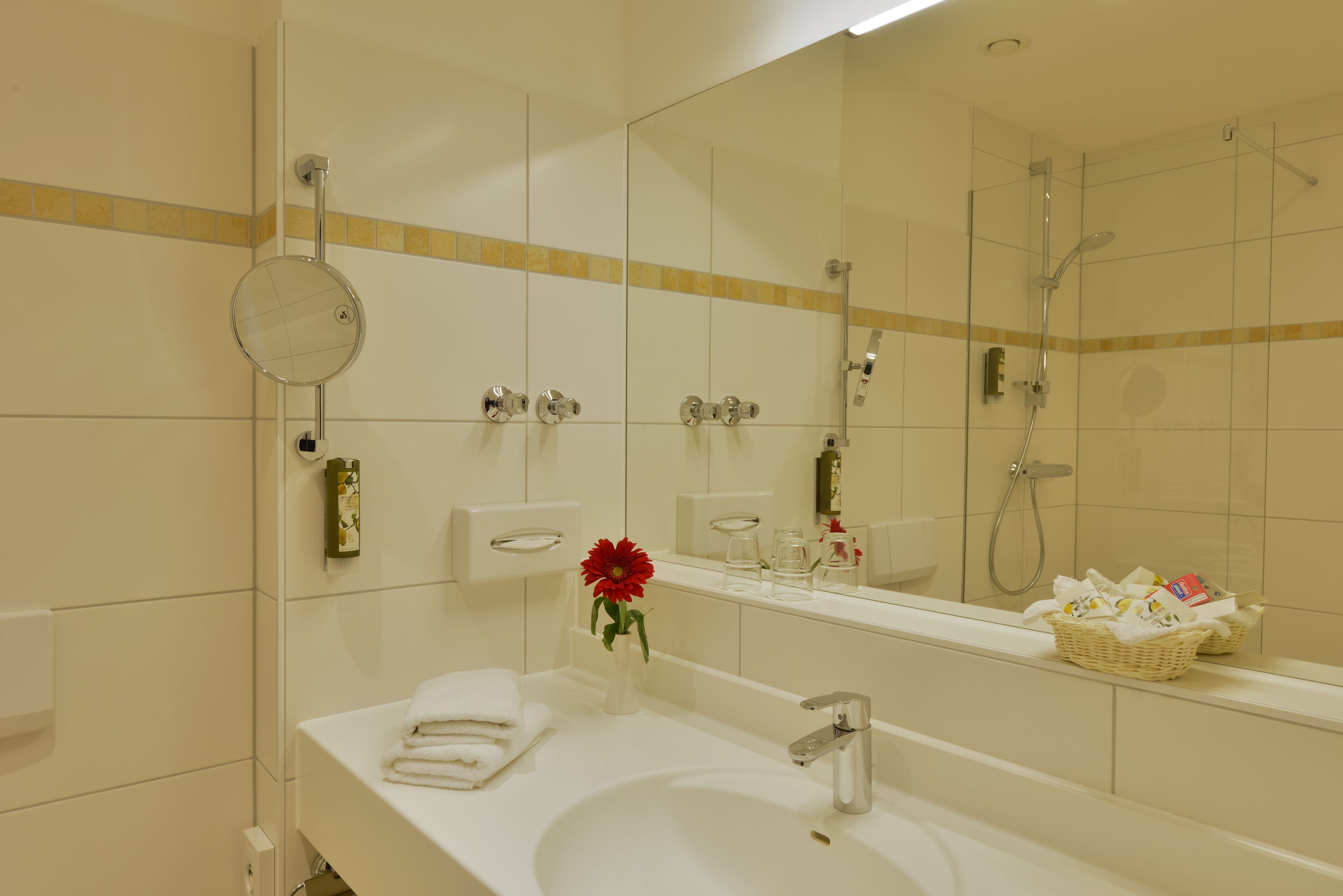 Un baño de hotel con lavamanos, espejo y ducha.