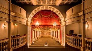 An ornate hallway with a grand archway, chandeliers, and a red draped curtain. - Hotel Der Lindenhof (Gotha)
