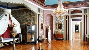 A grand room with a wooden parquet floor, ornate chandeliers, and classical decor including a mirror, candelabras, and a canopy bed. - Hotel Der Lindenhof (Gotha)